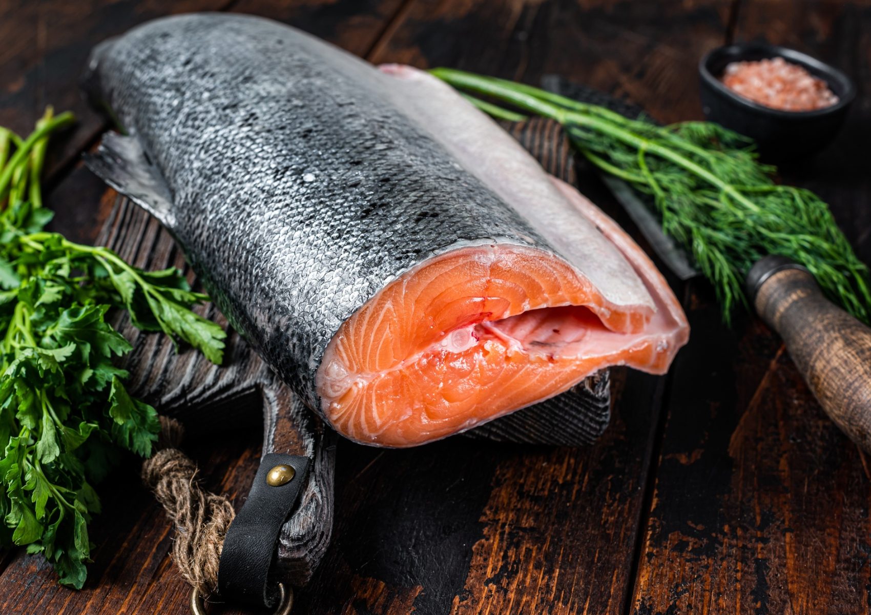 Big piece of Raw cut salmon fish on a wooden cutting board with chef knife.